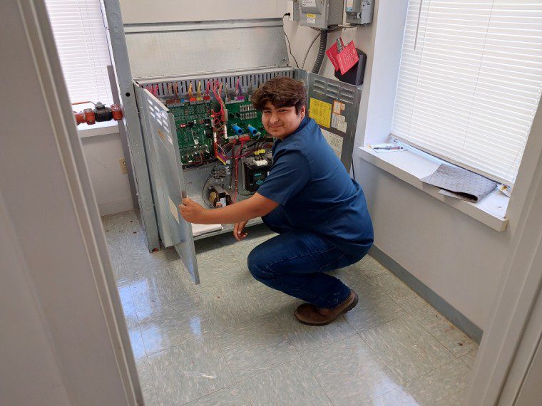 A person kneeling down in front of an electrical panel.